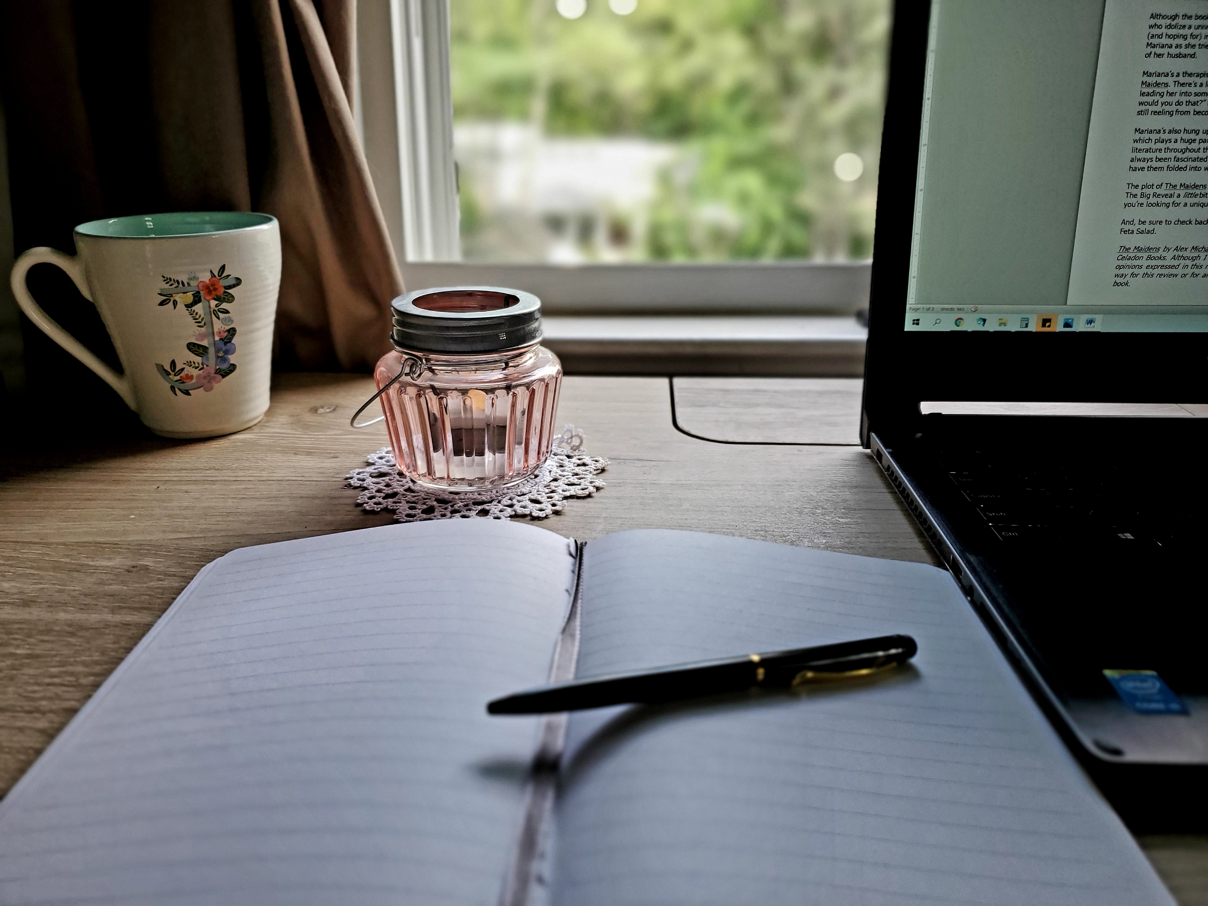 journal, pen, laptop, candle in front of window